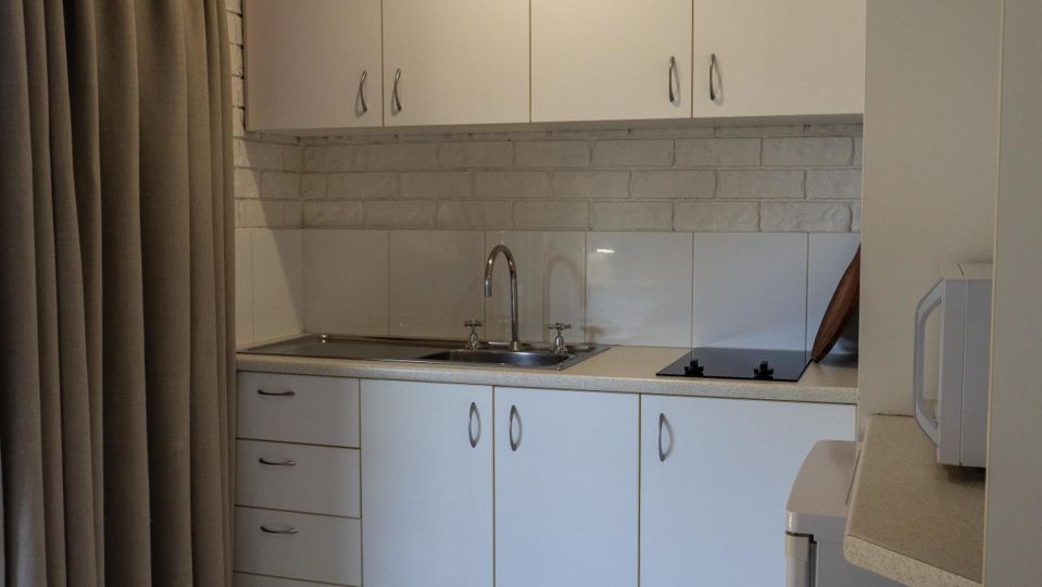 Close-up of a studio unit kitchenette at Dicky Beach Holiday Park, with a sink, cooktop and white cabinetry.